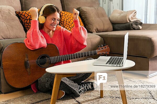 Frau  die zu Hause mit Online-Kursen am Computer Gitarre spielen lernt  lächelt  weil sie das Lied gut gespielt hat