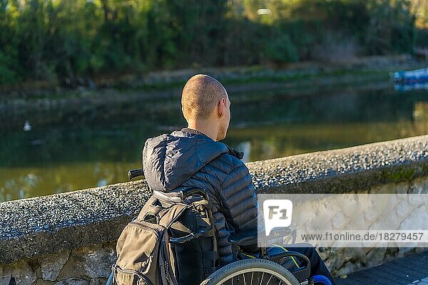 Eine behinderte Person im Rollstuhl in einem Park bei Sonnenuntergang am Fluss