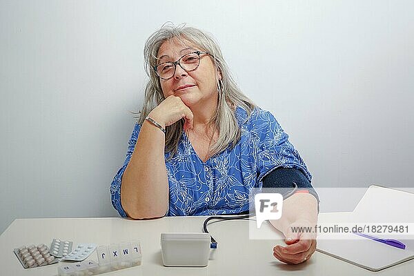 Ältere weißhaarige Frau mit Brille  die zu Hause ihren Blutdruck misst  mit weißem Hintergrund