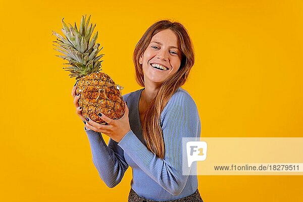 Mädchen lächelnd mit einer Ananas in Sonnenbrille in einem Studio auf einem gelben Hintergrund  gesund  Sommer