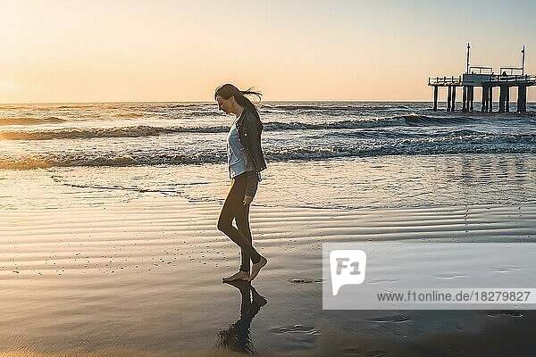 Eine einsame Frau am Strand  die bei Sonnenaufgang barfuß am Ufer entlang läuft. Raum kopieren