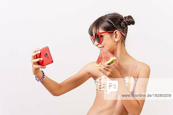 Girl with sunglasses enjoying the summer eating a watermelon  making a selfie with the phone. White background