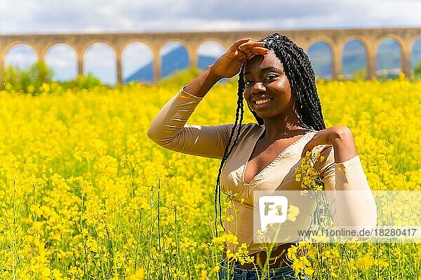 Lifestyle  portrait of a black ethnic girl with braids looking at camera  trap music dancer  in a field of yellow flowers