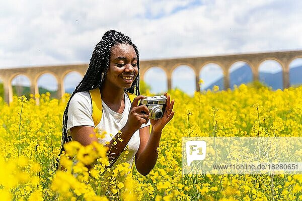Fotografieren von Blumen mit einer alten Kamera  ein schwarzes ethnisches Mädchen mit Zöpfen  eine Reisende  in einem Feld mit gelben Blumen