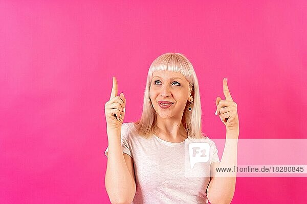 Blondes kaukasisches Mädchen Studioaufnahme auf rosa Hintergrund  Kopierraum  lächelnd nach oben zeigend
