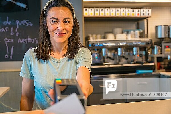 A brunette caucasian waitress smiling handing over the dataphone to charge with the customer's credit card contact