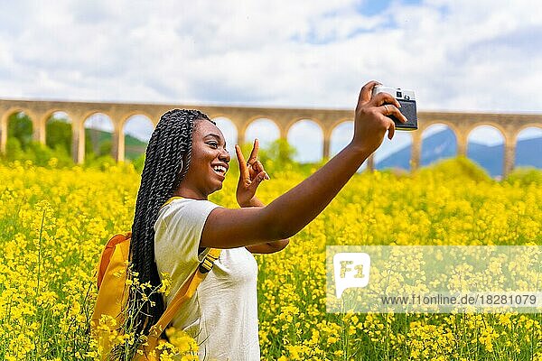 Selfie in der Natur mit einer Vintage-Kamera  ein Mädchen schwarzer Ethnie mit Zöpfen  eine Reisende  in einem Feld von gelben Blumen