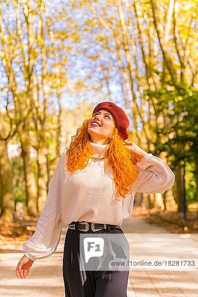 Red-haired woman in a beret walking through a city forest park at sunset  vertical photo