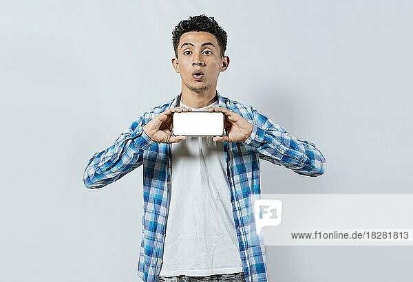 Erstaunlicher junger Mann zeigt Anzeige auf Handy. Überrascht schöner Mann zeigt den horizontalen Bildschirm seines Handys  Überrascht Mann mit Brille zeigt leeren Bildschirm des Smartphones