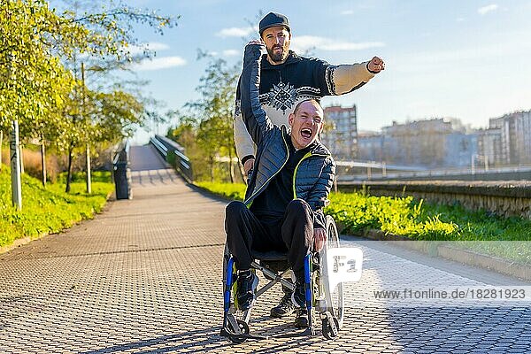 Behinderte Person im Rollstuhl mit Freund überglücklich  lächelnd  mit erhobenen Armen genießend  vistoria  das Leben genießend