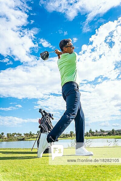 A player playing golf on the golf course  hitting the ball next to a lake  vertical photo