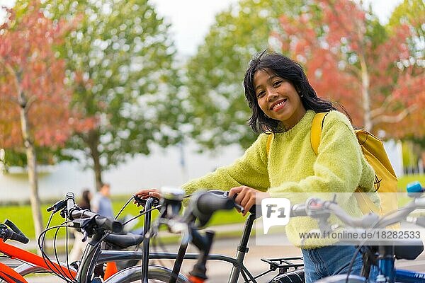 Porträt einer lächelnden asiatischen Studentin  die ein Fahrrad auf einem College-Campus parkt