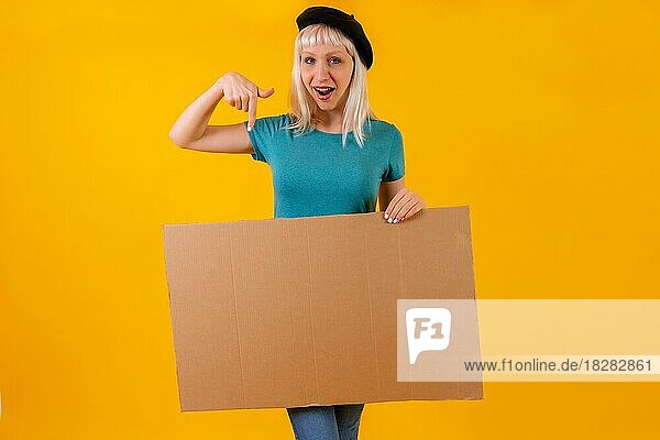 Zeigen lächelnd Karton Werbeplakat  blonde kaukasische Mädchen auf gelben Studio Hintergrund