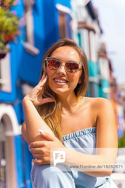 Portrait of attractive young blonde woman in sunglasses in a posed  behind blue colorful facade