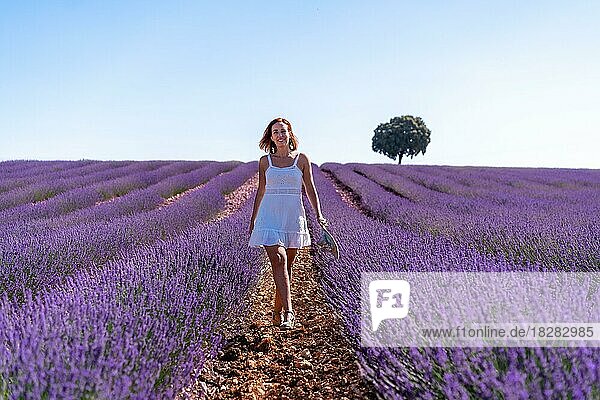 Eine lächelnde Frau in einem sommerlichen Lavendelfeld in einem weißen Kleid genießt die Natur