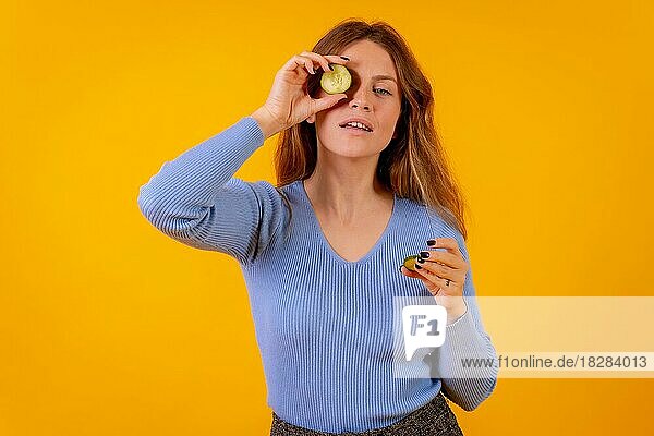 Vegane Frau mit einer Gurkenscheibe auf dem Auge auf gelbem Hintergrund  vegetarisches Leben