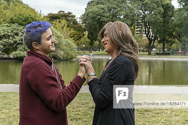 Transgender-Frau und ihr schwuler Sohn halten sich an den Händen und schauen sich liebevoll in einem Park an