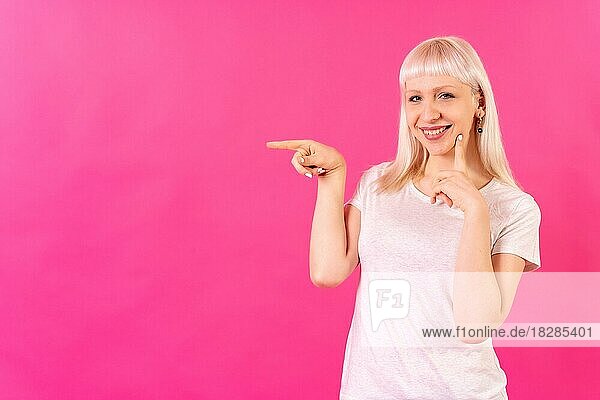 Blondes kaukasisches Mädchen Studioaufnahme auf rosa Hintergrund  Kopierraum  lächelnd nach links zeigend