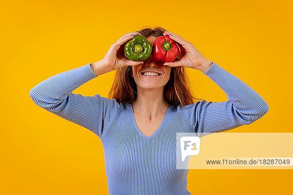 Vegetarische Frau in einem Porträt mit Paprika in den Augen auf einem gelben Hintergrund  gesunde Ernährung