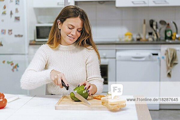 Vegetarische Frau  die zu Hause in der Küche ein Gemüsesandwich zubereitet und grüne Paprika schneidet