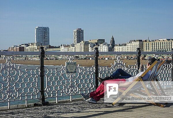 Touristen sitzen auf Liegestühlen am Pier von Brighton. Brighton  Sussex  England  Großbritannien  Europa