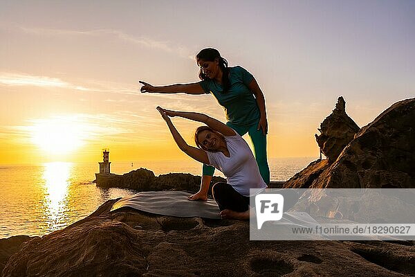 A yoga instructor working with the student in nature by the sea at sunset  healthy and naturist life  outdoor pilates