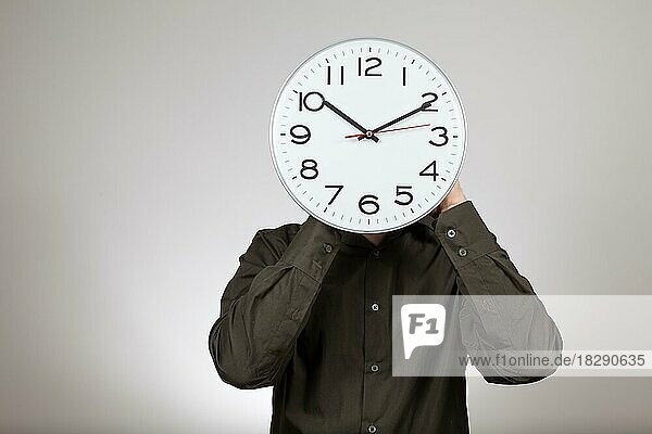 Symbolbild Arbeitszeit  Mann hält sich eine Uhr vor sein Gesicht