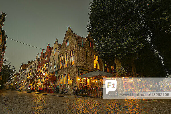 Belgium  West Flanders  Bruges  Cobblestone street stretching in front of sidewalk cafe and row of town houses at dusk