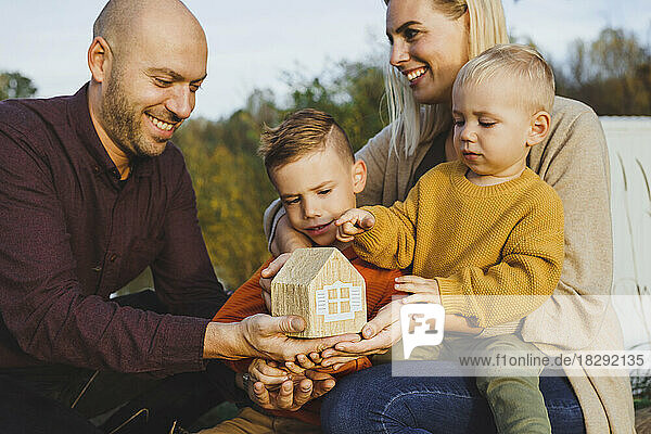 Happy parents with children holding model house in nature