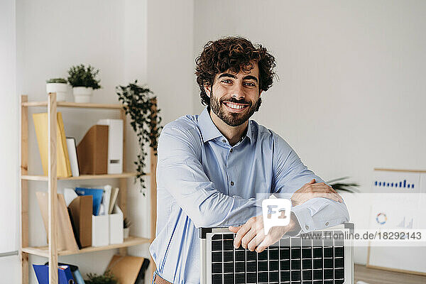 Happy young businessman with solar panel standing in office