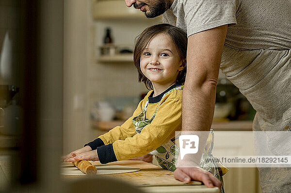 Lächelnder Sohn rollt mit Vater in der heimischen Küche Teig