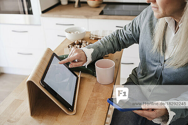Woman using tablet PC sitting at table in kitchen