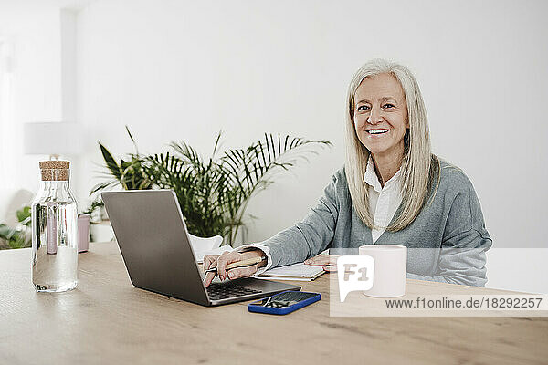 Happy mature freelancer sitting with laptop at desk
