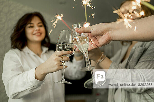 Happy friends enjoying with glasses of champagne and sparklers at home