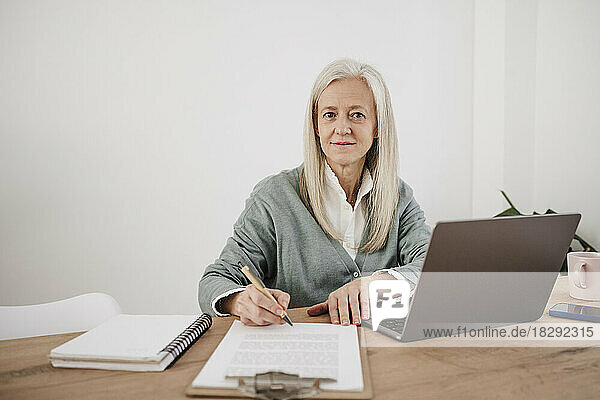 Smiling freelancer with documents and laptop sitting at desk