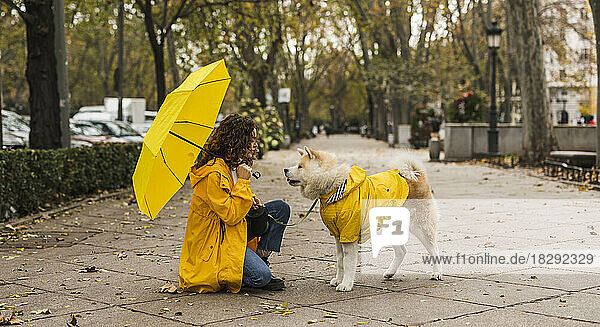 Young woman holding umbrella and crouching with dog at footpath