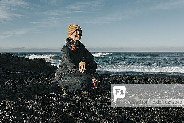 Smiling woman crouching on sand at Janubio Beach  Lanzarote  Canary Islands  Spain