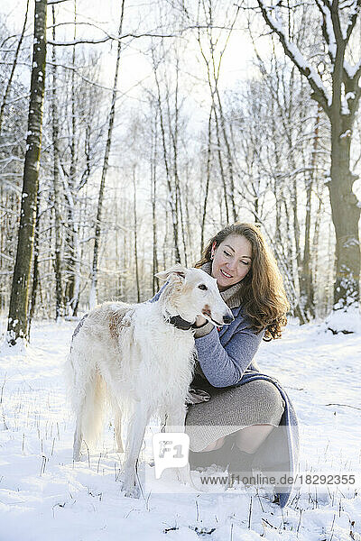 Happy mature woman stroking greyhound dog in winter park