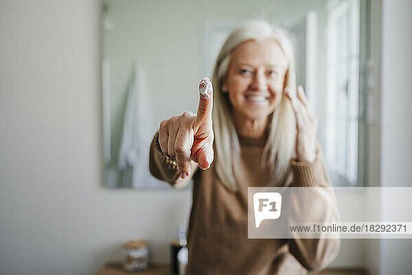 Smiling mature woman with moisturizer on finger in bathroom