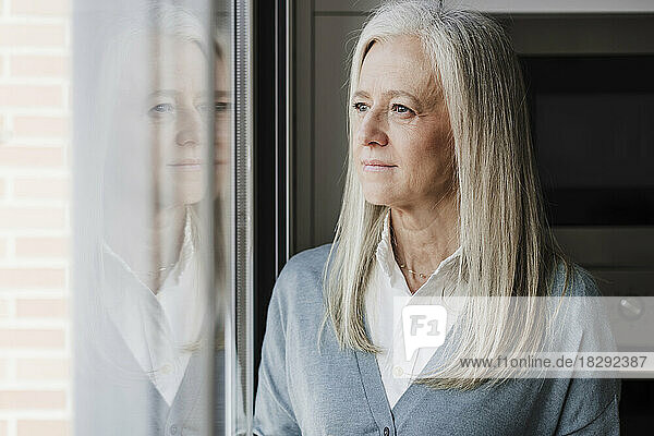 Thoughtful mature woman with gray hair by window at home