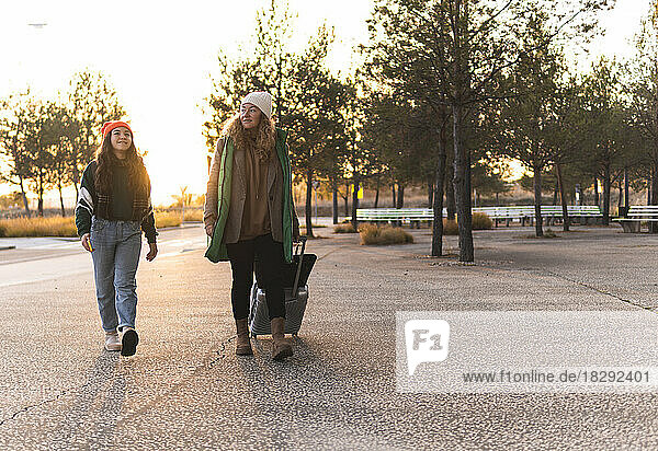 Mutter und Mädchen gehen bei Sonnenuntergang mit Gepäck auf dem Fußweg