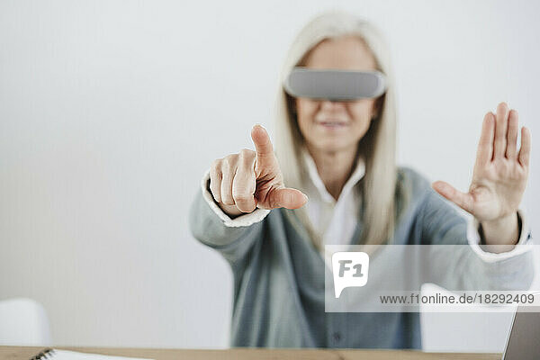 Reife Frau mit VR-Brille gestikuliert vor der Wand