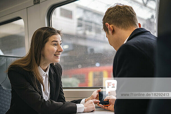 Happy businesswoman sharing smart phone to colleague in train