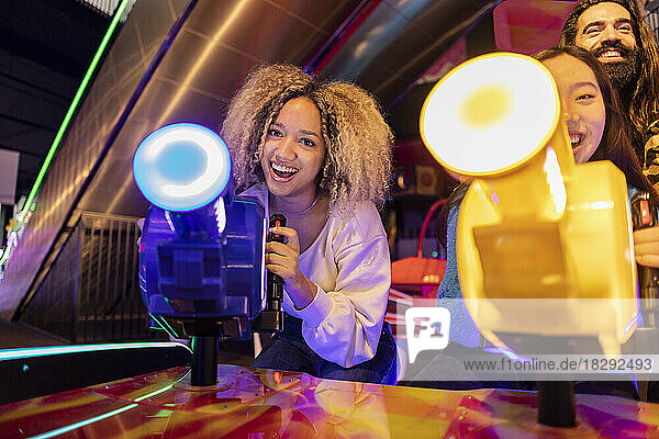 Happy young woman with friends playing video game in amusement arcade