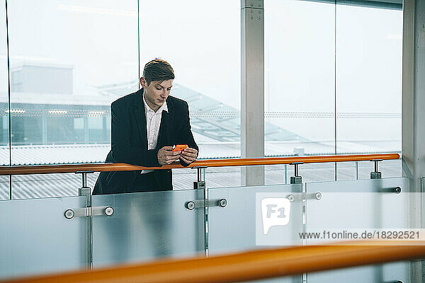 Young businessman using smart phone leaning on railing