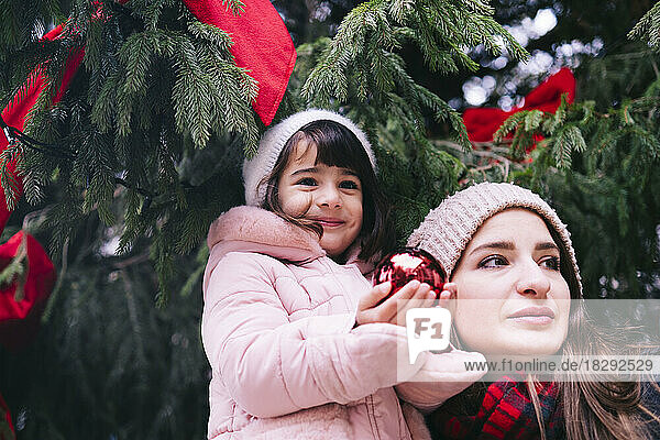 Mother with smiling daughter holding Christmas bauble