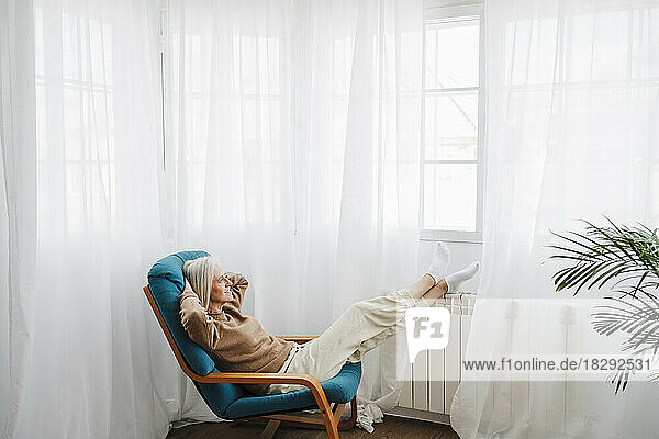 Woman relaxing on armchair in front of window at home