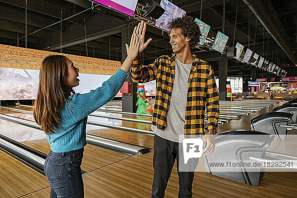 Young woman giving high five to friend at bowling alley