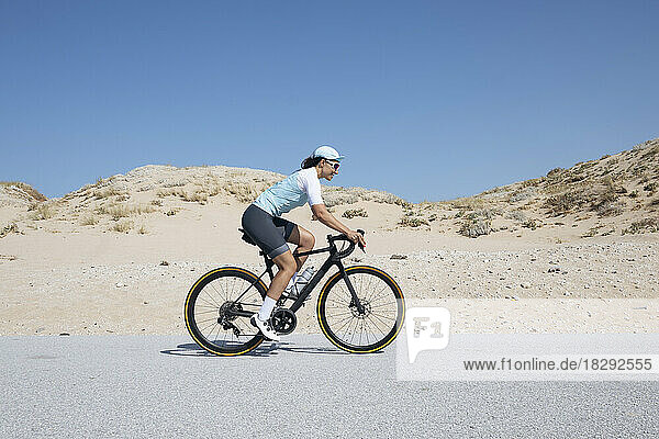 Mature cyclist riding bicycle on road by sand dunes