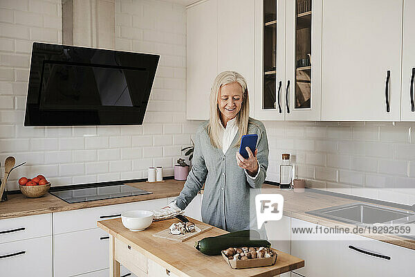Happy mature woman using smart phone in kitchen